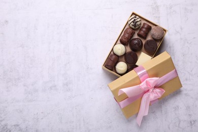 Photo of Open box with delicious chocolate candies on white table, top view. Space for text