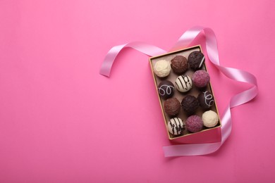 Photo of Open box with delicious chocolate candies and ribbon on pink background, top view. Space for text