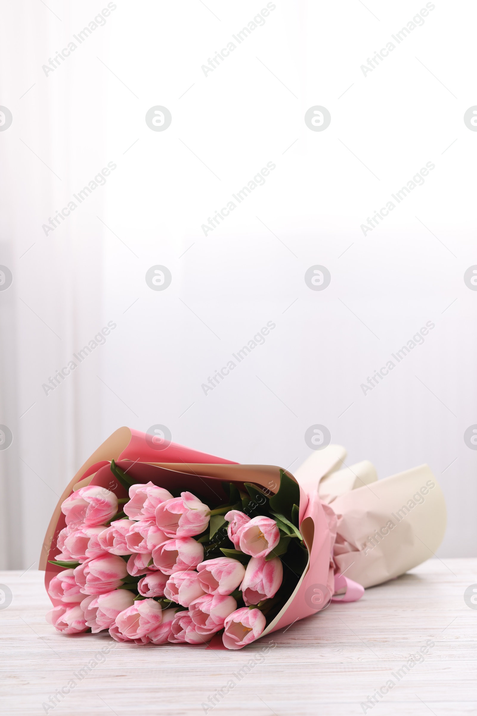 Photo of Beautiful bouquet of fresh pink tulips on white wooden table indoors. Space for text