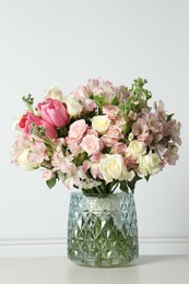 Photo of Beautiful bouquet of fresh flowers in vase on table near white wall