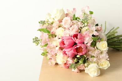 Photo of Beautiful bouquet of fresh flowers on wooden table near light wall. Space for text