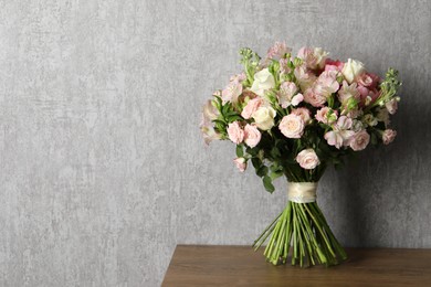 Photo of Beautiful bouquet of fresh flowers on wooden table near grey wall, space for text