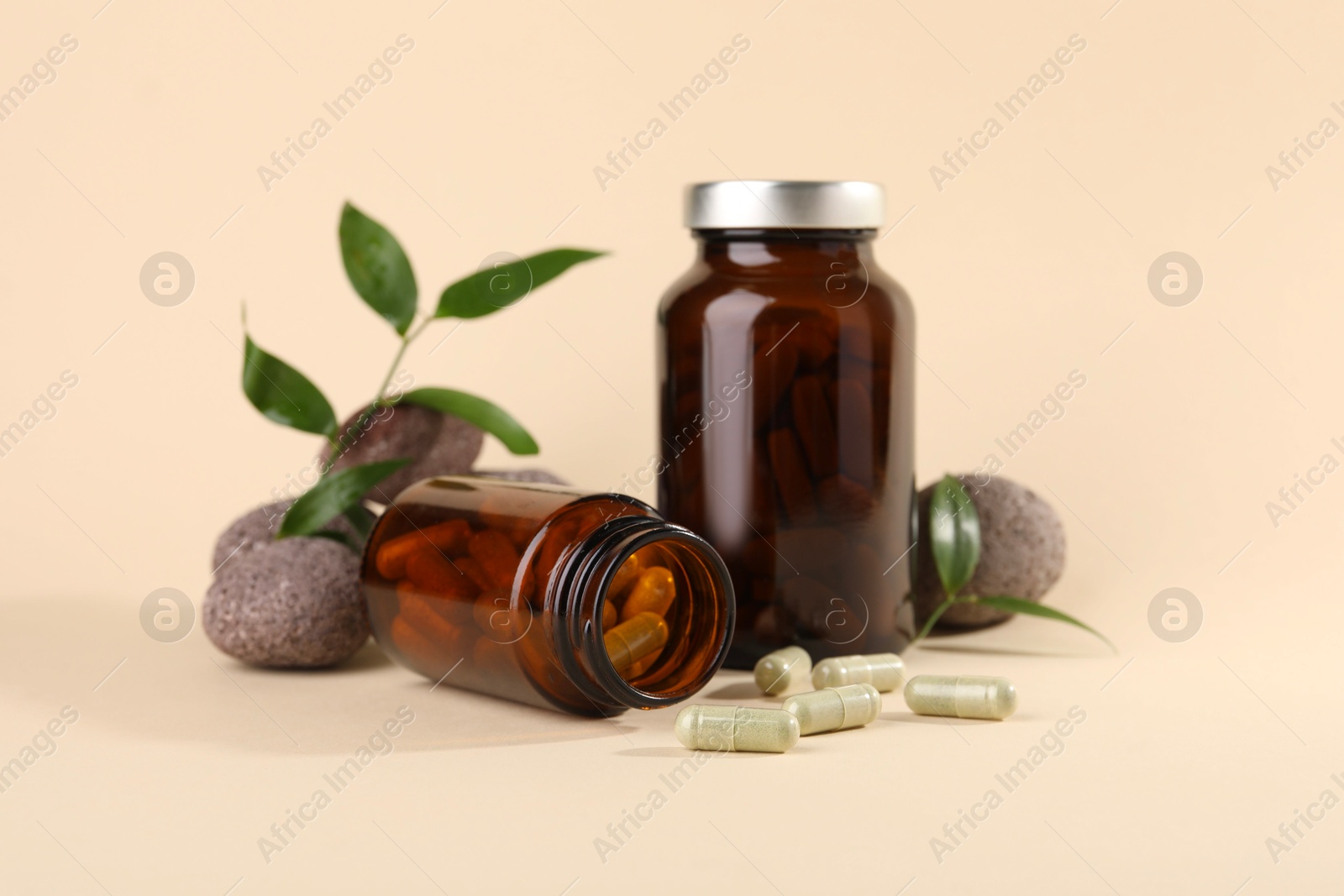 Photo of Medical bottles with pills, stones and green leaves on beige background