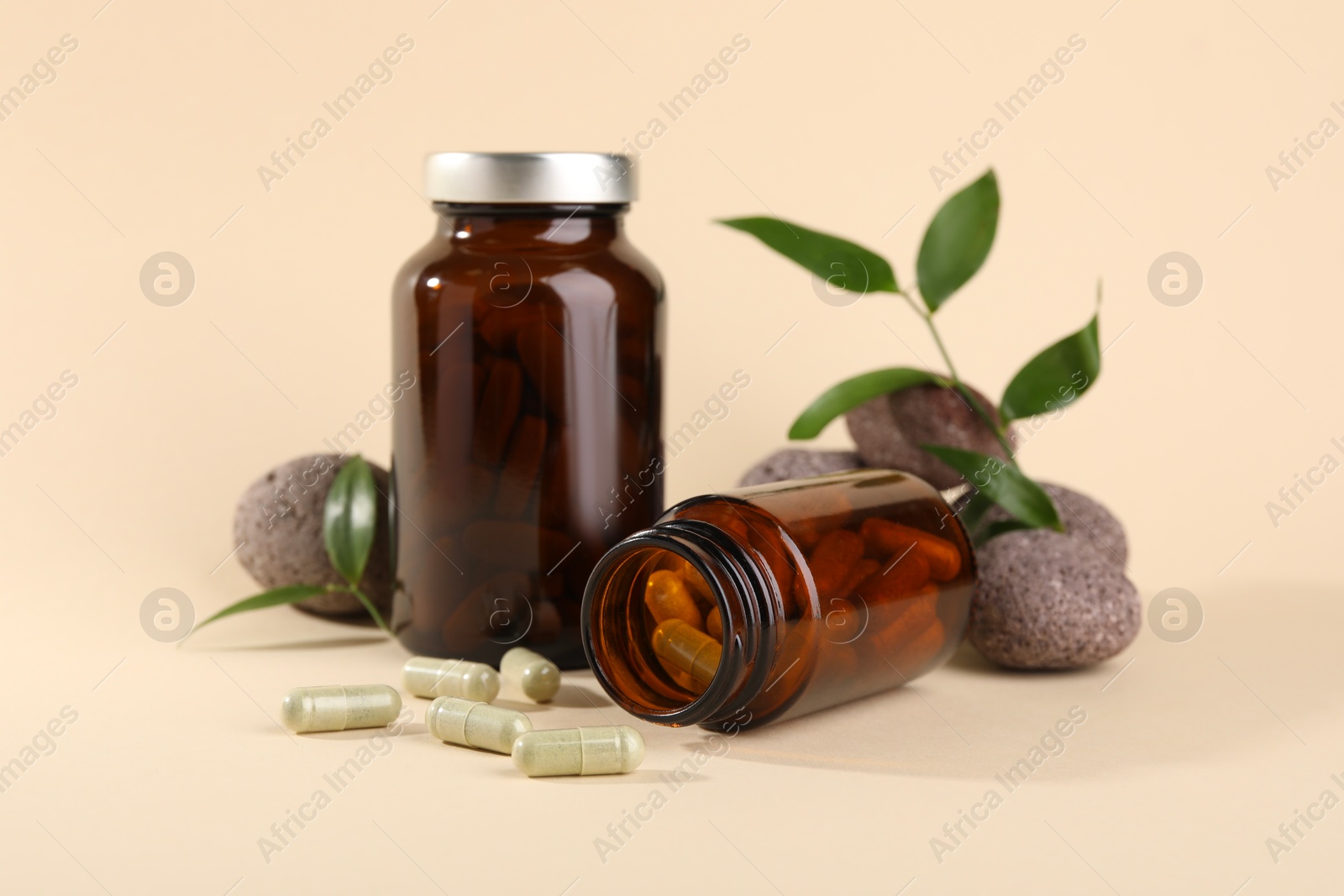 Photo of Medical bottles with pills, stones and green leaves on beige background