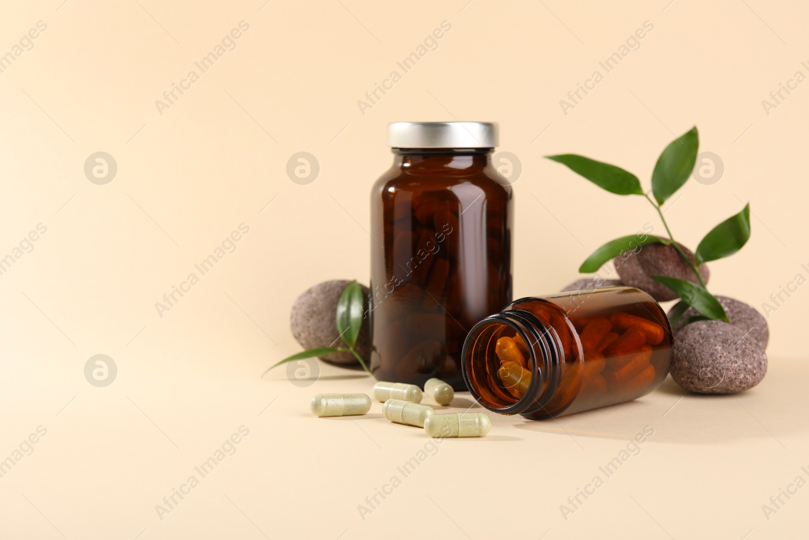 Photo of Medical bottles with pills, stones and green leaves on beige background, space for text