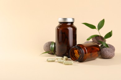 Photo of Medical bottles with pills, stones and green leaves on beige background, space for text