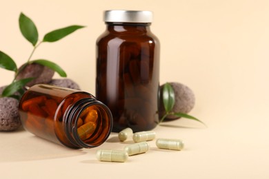 Photo of Medical bottles with pills, stones and green leaves on beige background, closeup