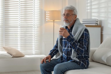 Photo of Lonely senior man with glass of water sitting on sofa at home. Space for text