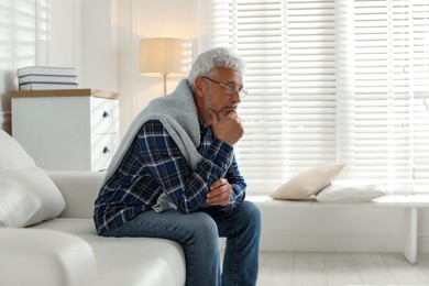 Photo of Lonely senior man sitting on sofa at home. Space for text