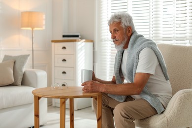 Photo of Lonely senior man with cup of drink at wooden table indoors