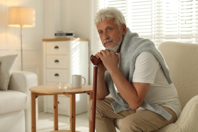 Photo of Lonely senior man with walking cane sitting in armchair at home