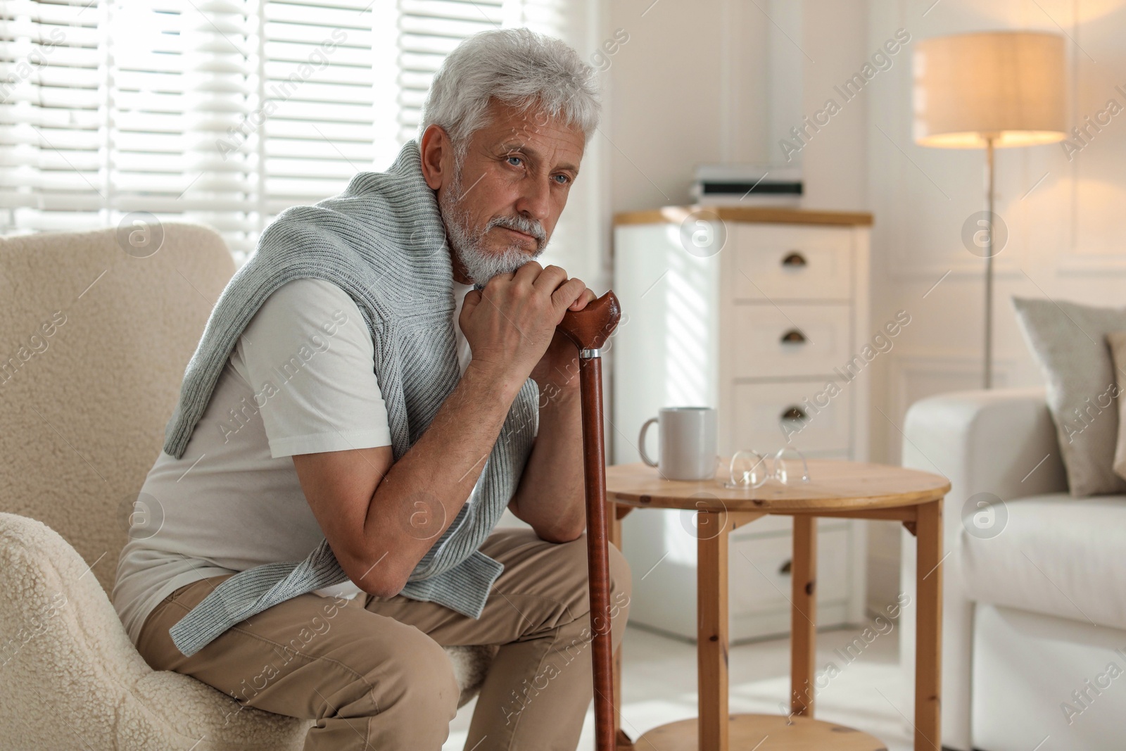 Photo of Lonely senior man with walking cane sitting in armchair at home