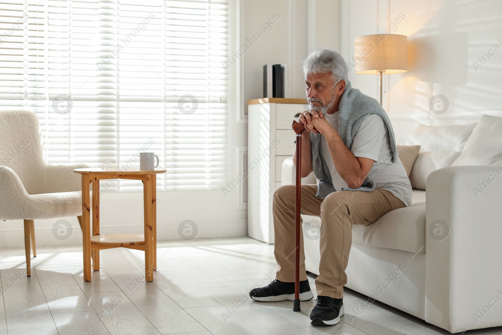 Photo of Lonely senior man with walking cane sitting on sofa at home