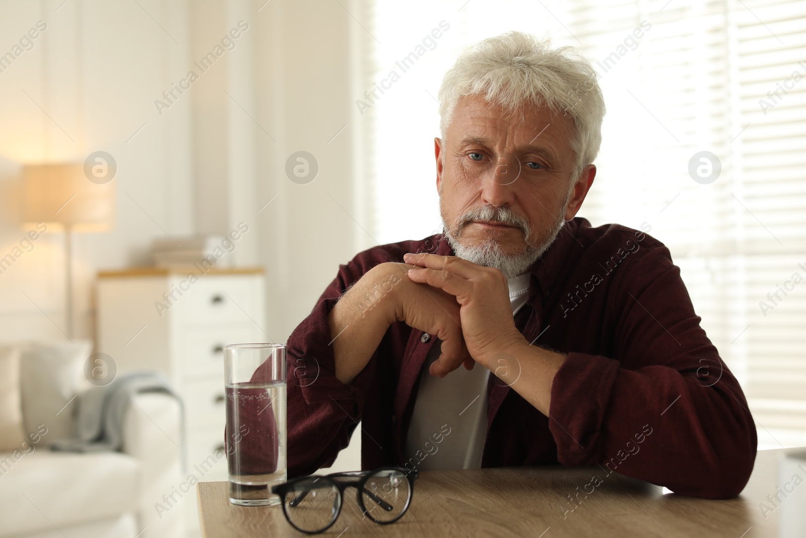 Photo of Sad senior man feeling lonely while sitting at wooden table indoors