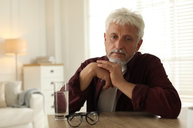 Photo of Sad senior man feeling lonely while sitting at wooden table indoors