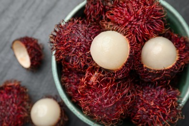 Photo of Delicious ripe rambutans in bowl on black table, top view