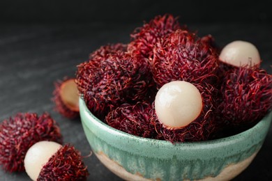 Photo of Delicious ripe rambutans in bowl on black table, closeup