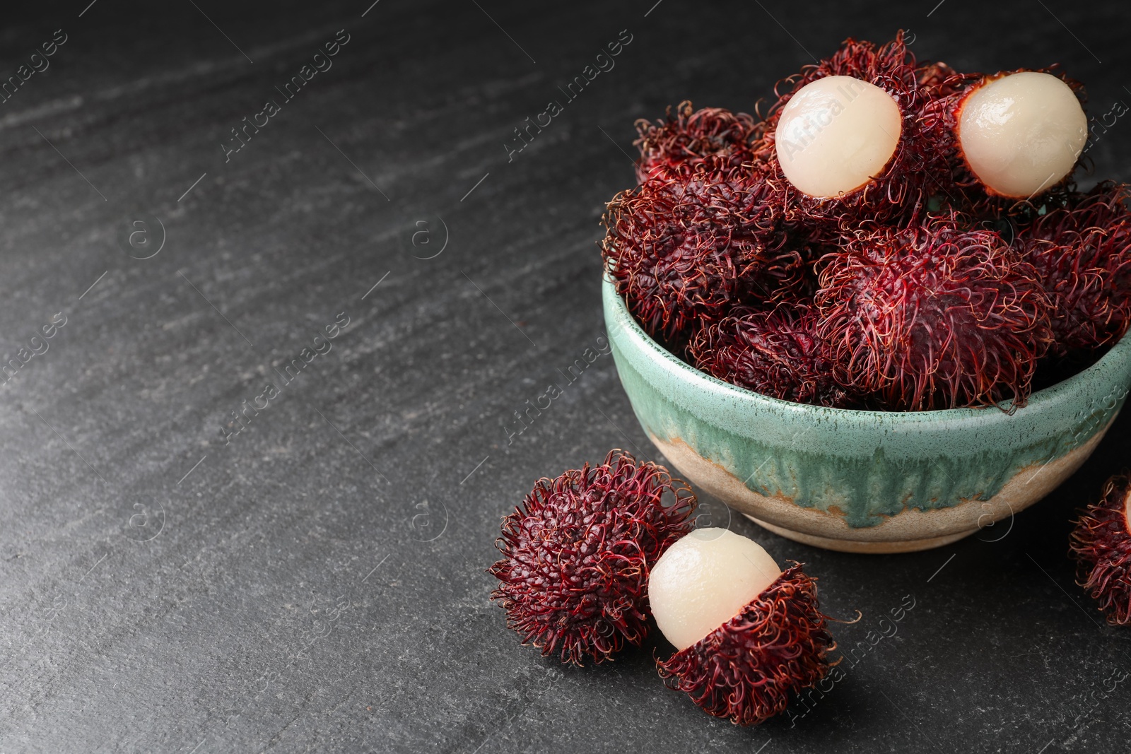 Photo of Delicious ripe rambutans in bowl on black table, closeup. Space for text