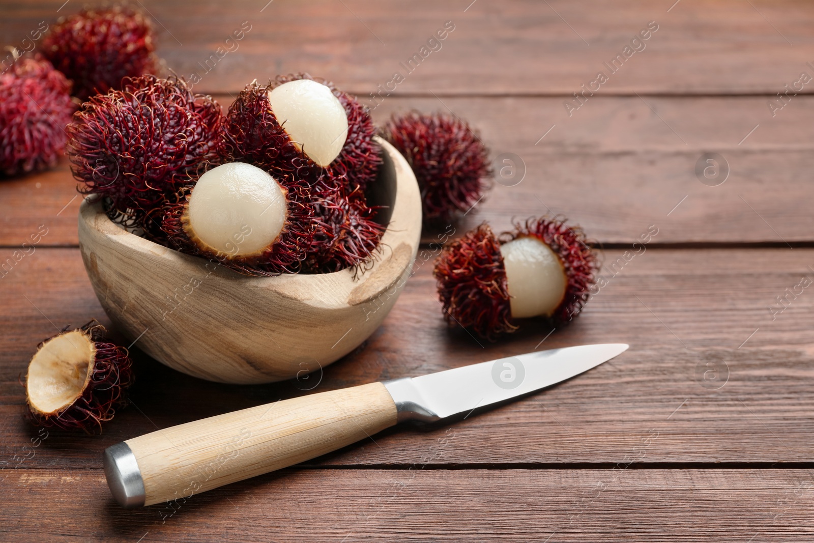 Photo of Delicious ripe rambutans in bowl and knife on wooden table, space for text