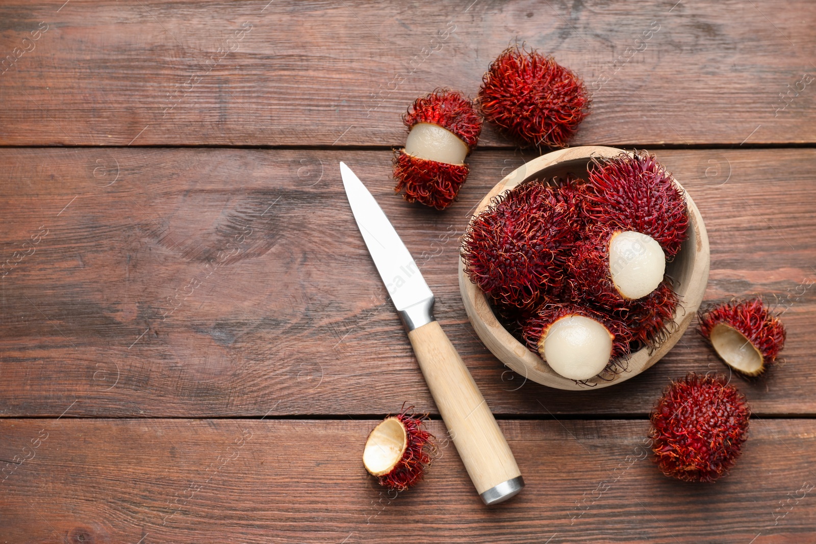 Photo of Delicious ripe rambutans in bowl and knife on wooden table, flat lay. Space for text