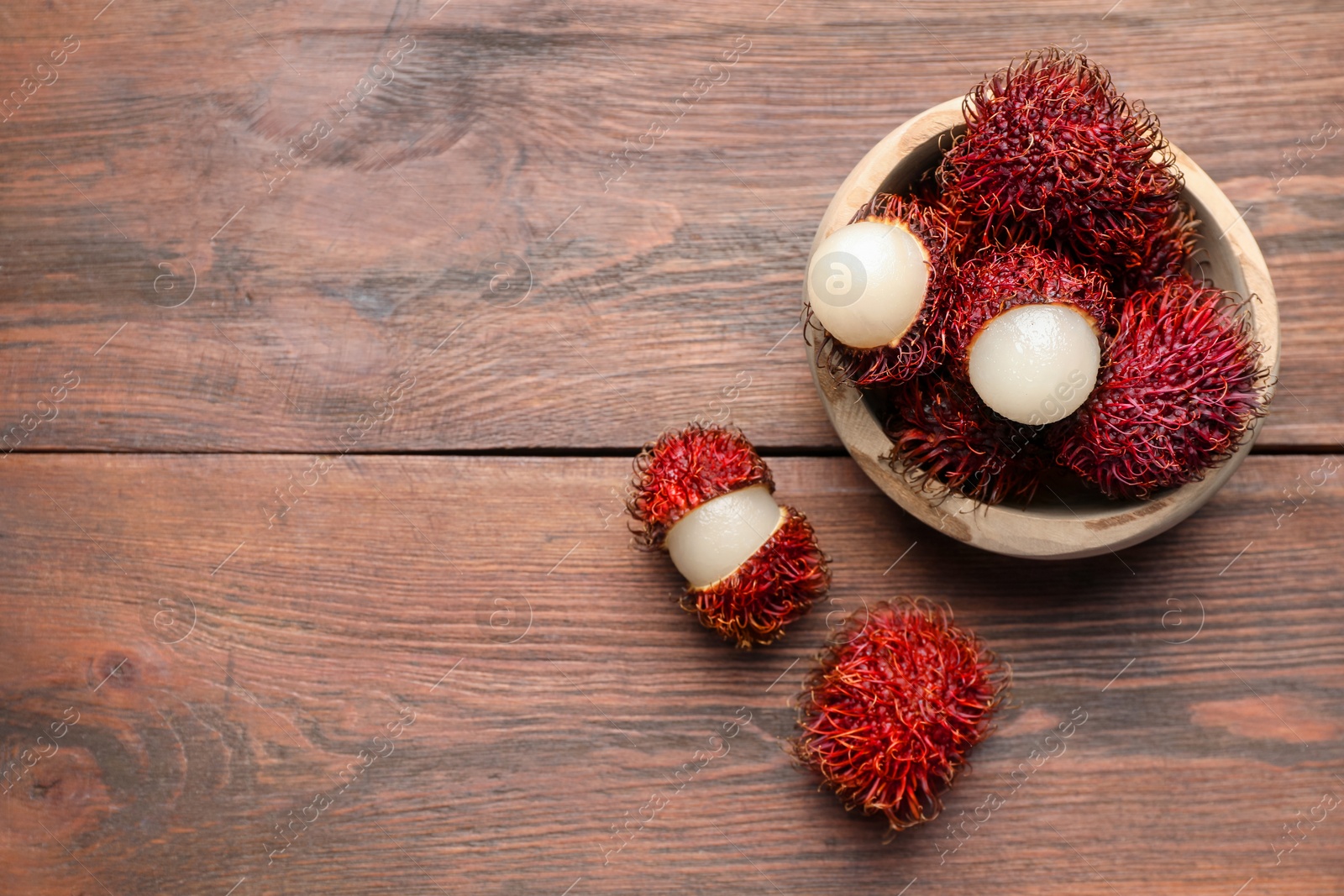 Photo of Delicious ripe rambutans in bowl on wooden table, top view. Space for text