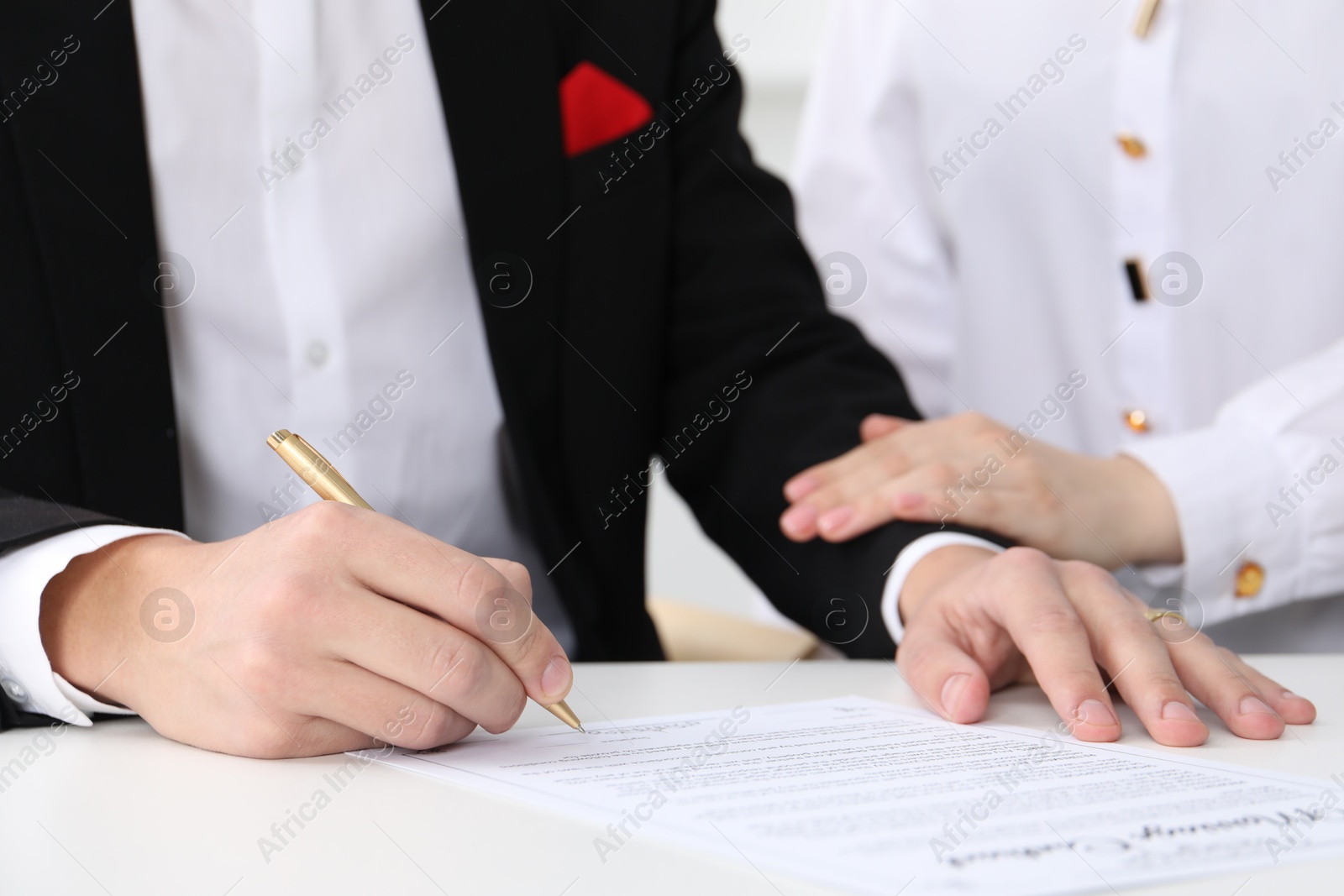 Photo of Newlyweds signing marriage contract at desk, closeup