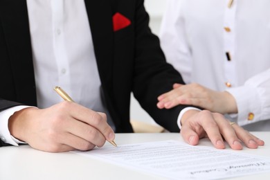 Photo of Newlyweds signing marriage contract at desk, closeup