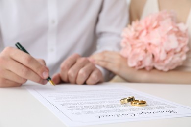 Photo of Newlyweds signing marriage contract and wedding rings on desk, selective focus