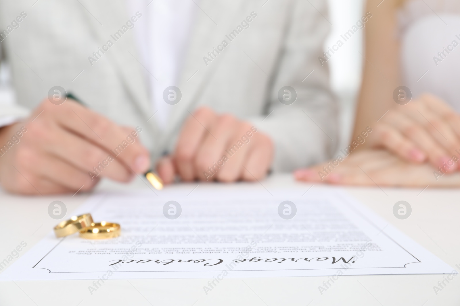 Photo of Newlyweds signing marriage contract and wedding rings on desk, selective focus