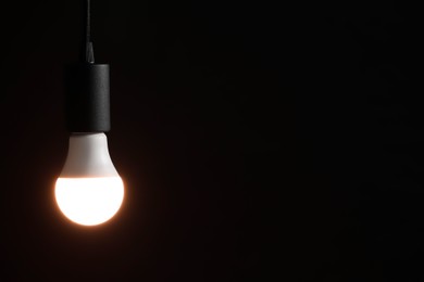 Photo of Glowing light bulb hanging on dark background. Space for text