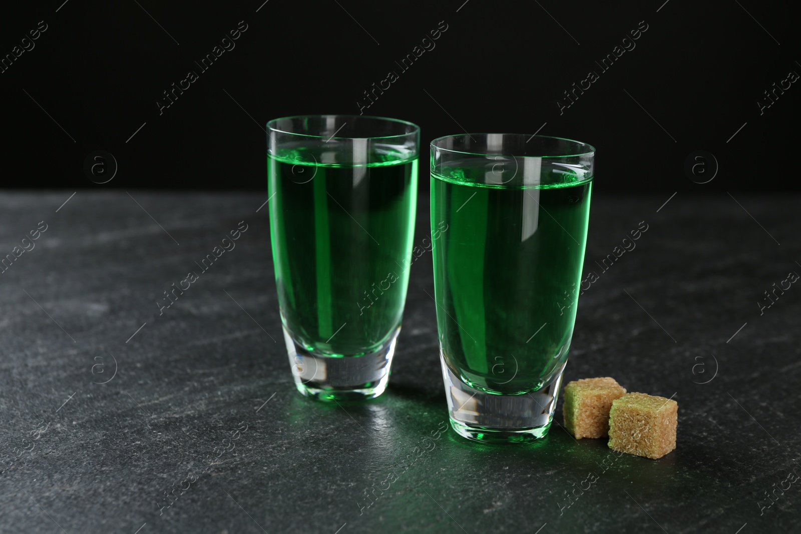 Photo of Absinthe in shot glasses and brown sugar on black table, space for text