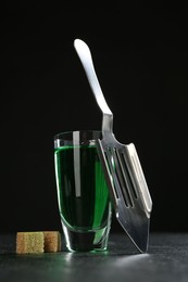 Photo of Absinthe in shot glass, brown sugar and slotted spoon on table against black background