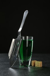 Photo of Absinthe in shot glass, brown sugar and slotted spoon on table against black background