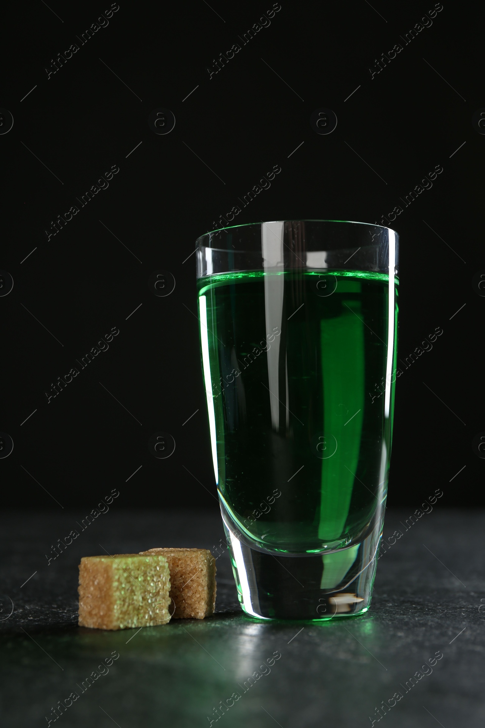 Photo of Absinthe in shot glass and brown sugar on table against black background