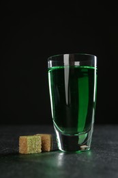 Photo of Absinthe in shot glass and brown sugar on table against black background