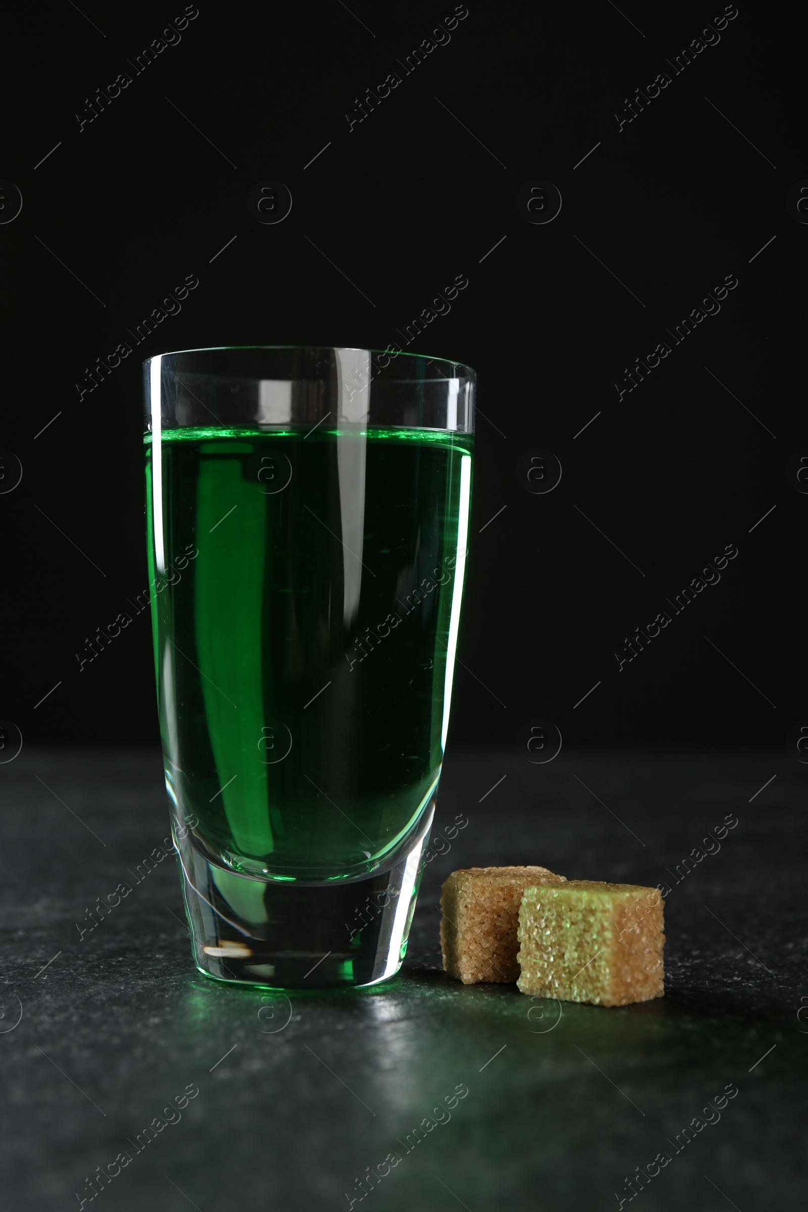 Photo of Absinthe in shot glass and brown sugar on table against black background