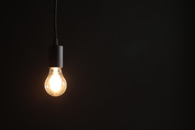 Photo of Glowing light bulb hanging on dark background. Space for text