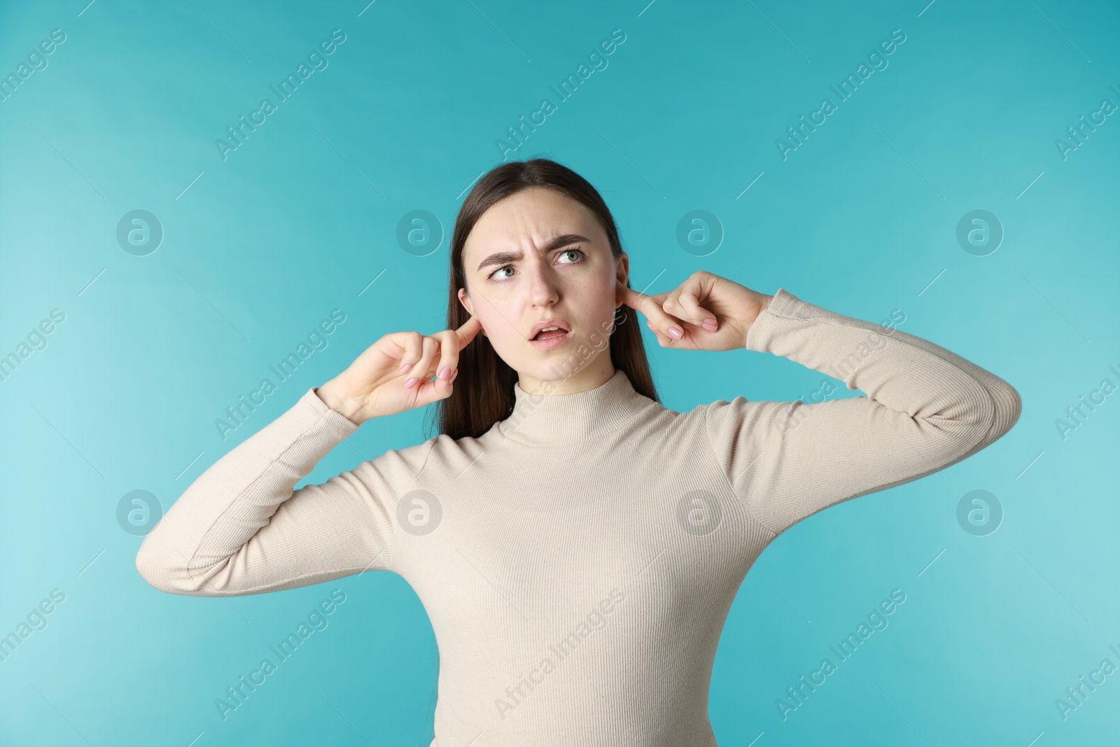 Photo of Frustrated woman covering her ears from loud noise on blue background