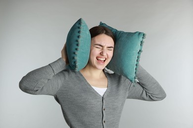 Photo of Distressed woman covering her ears with pillows from loud noise on light grey background