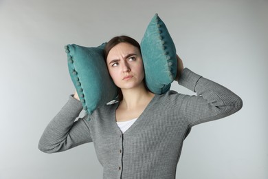 Photo of Distressed woman covering her ears with pillows from loud noise on light grey background