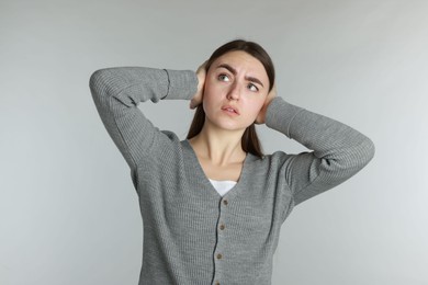 Distressed woman covering her ears from loud noise on light grey background