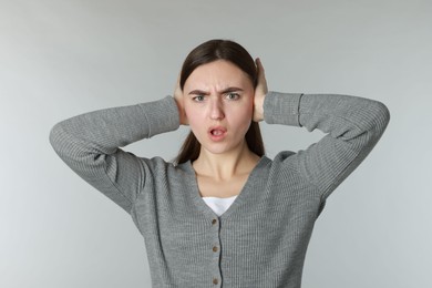 Photo of Distressed woman covering her ears from loud noise on light grey background