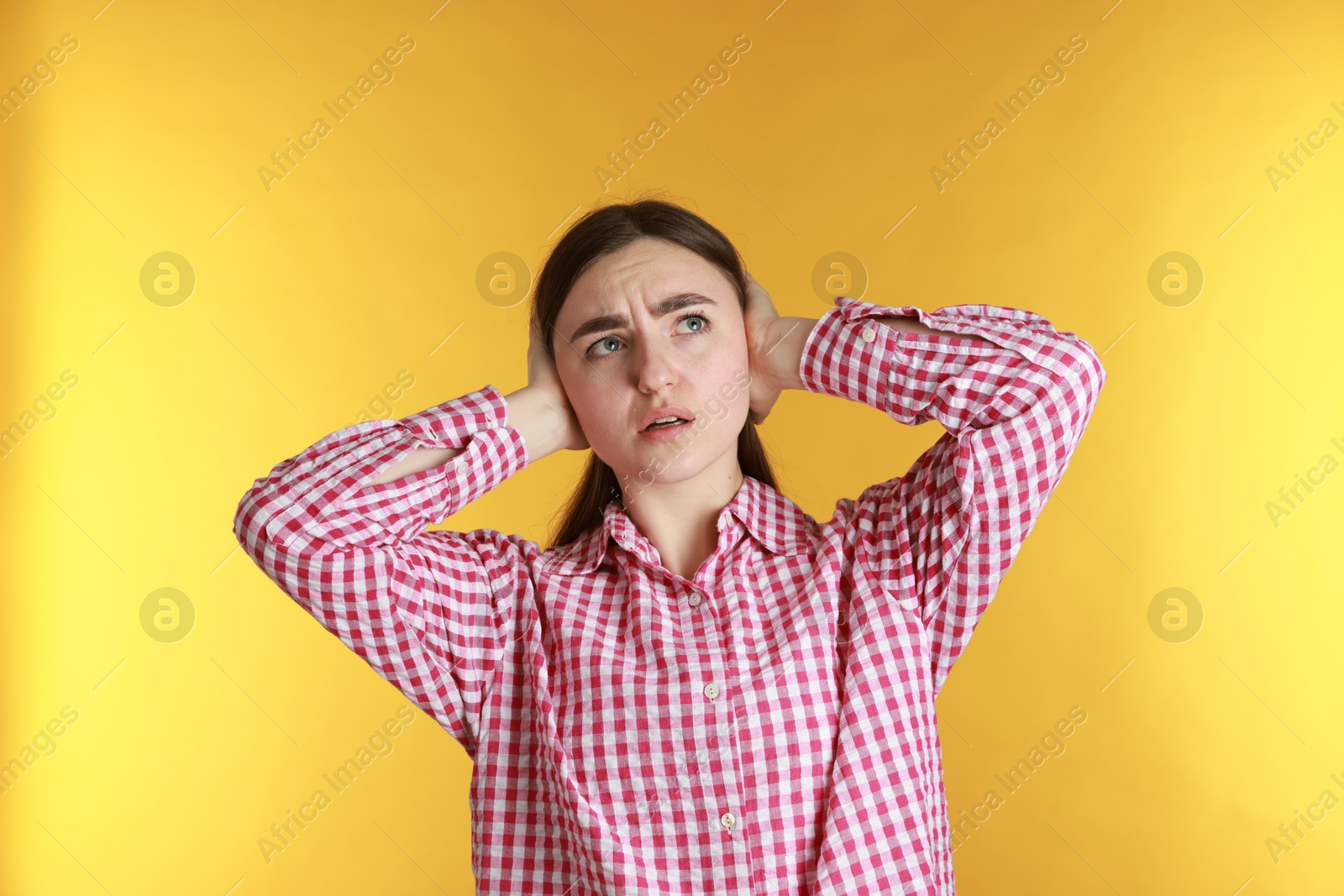 Photo of Distressed woman covering her ears from loud noise on yellow background