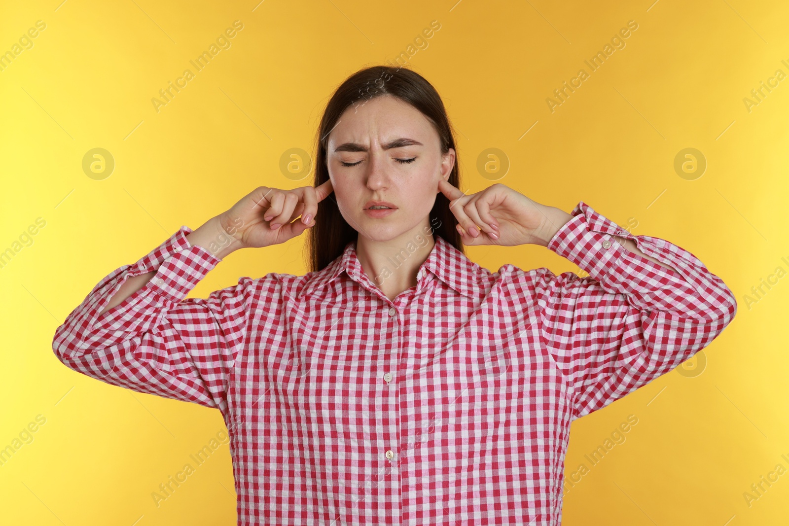 Photo of Distressed woman covering her ears from loud noise on yellow background