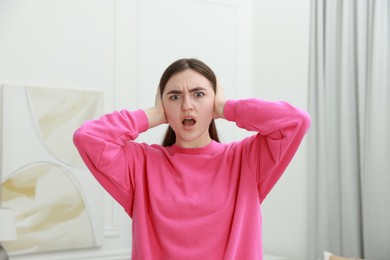 Photo of Annoyed woman covering her ears from loud noise at home