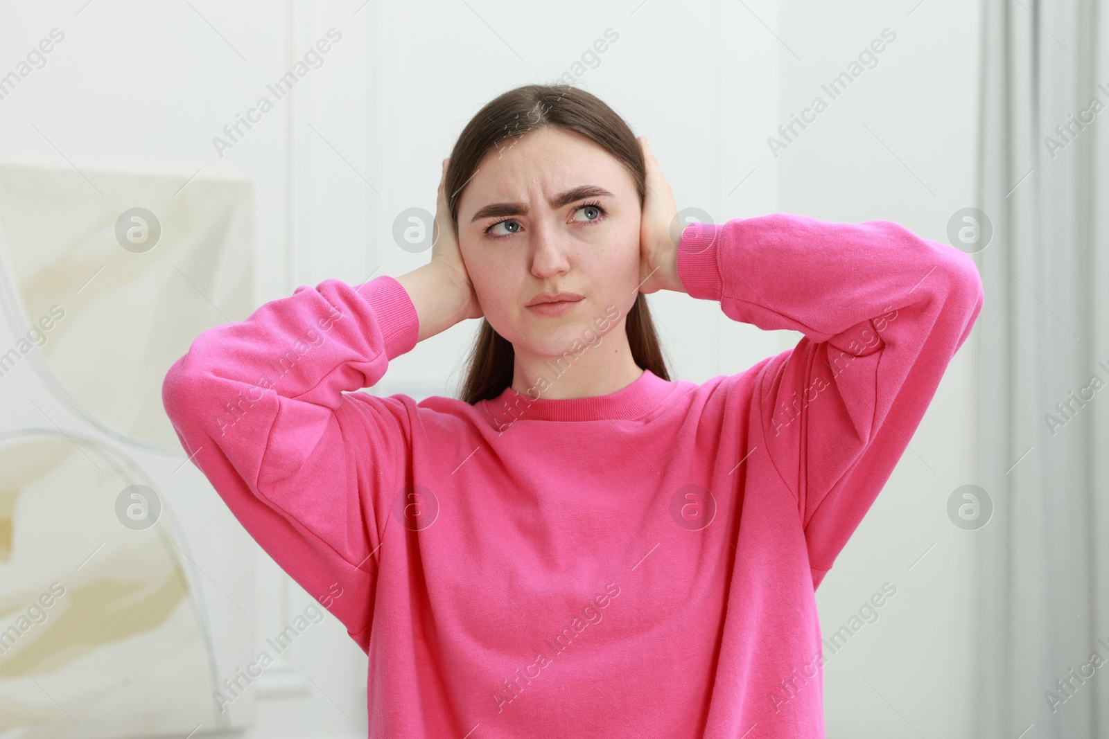 Photo of Annoyed woman covering her ears from loud noise at home