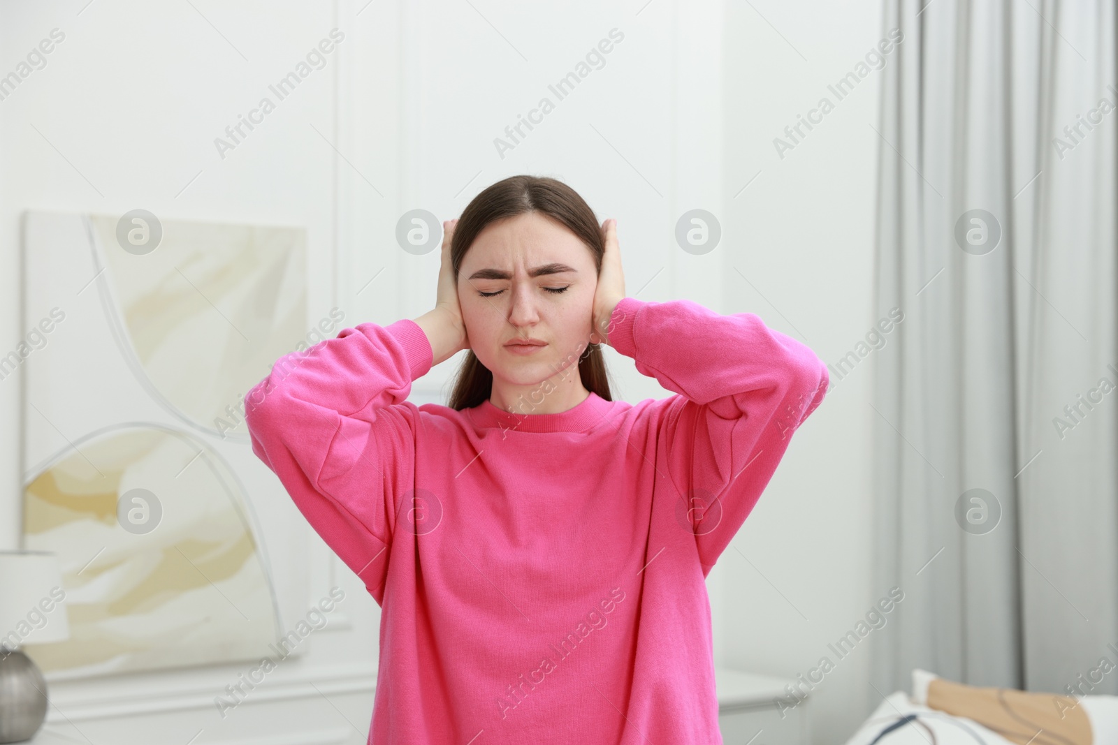 Photo of Annoyed woman covering her ears from loud noise at home