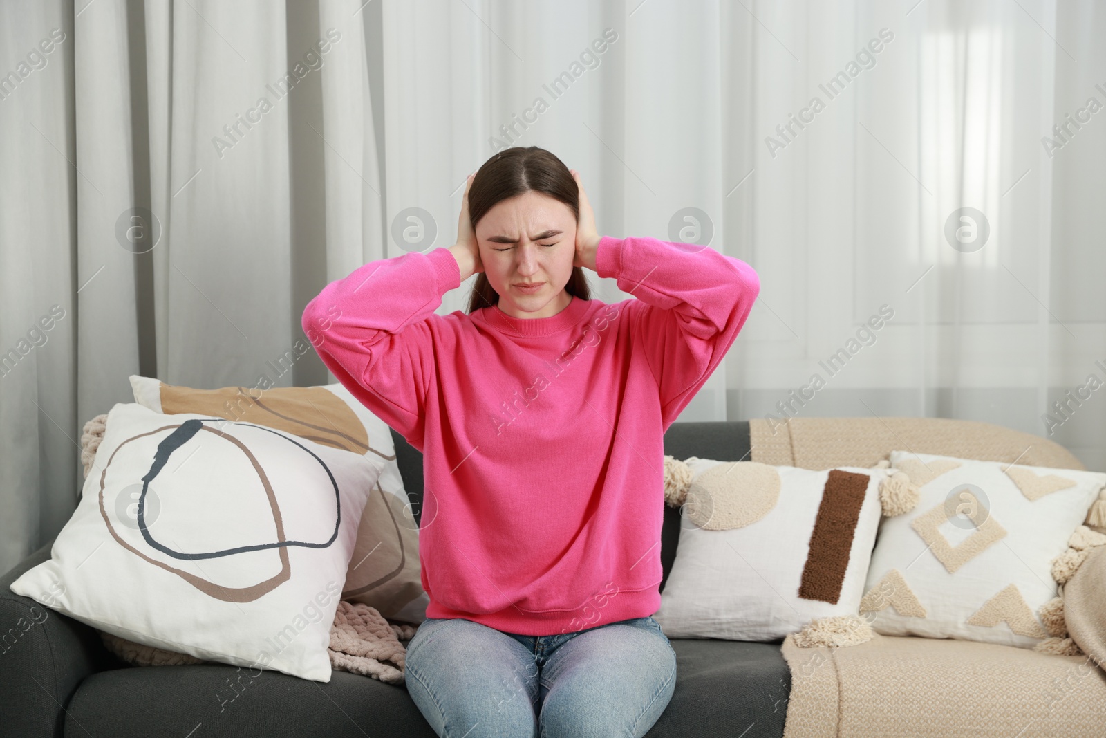 Photo of Annoyed woman covering her ears from loud noise at home