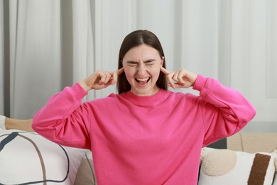 Photo of Annoyed woman covering her ears from loud noise at home