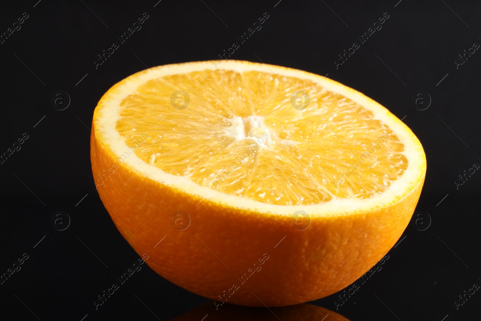 Photo of Half of fresh orange on black mirror surface, closeup